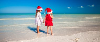 Little cute girls in Christmas hats on the exotic beach
